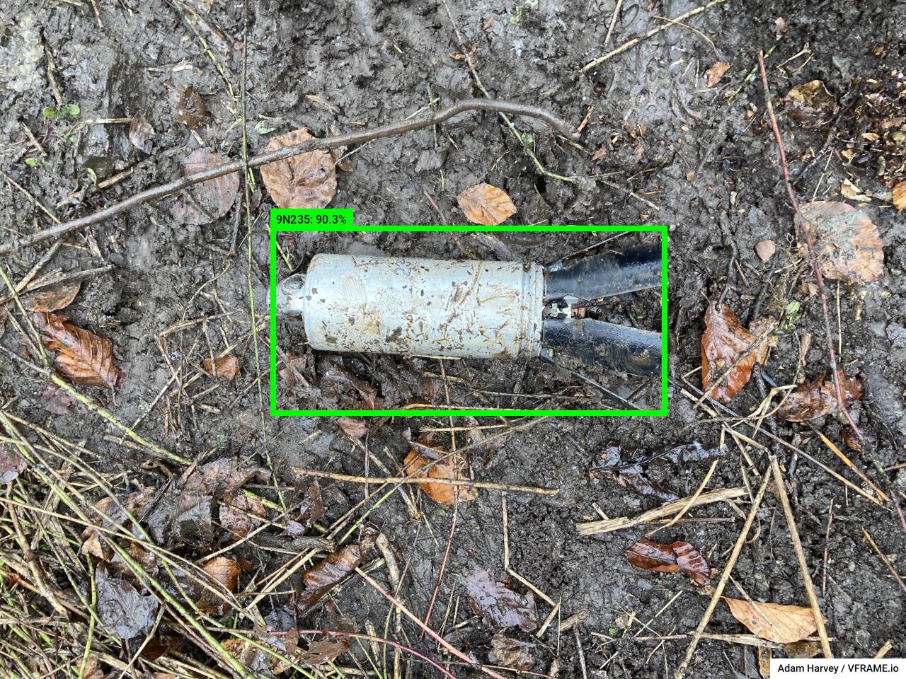 A free from explosive (FFE) 9N235/9N210 submunition photographed at close range in wet forest terrain
